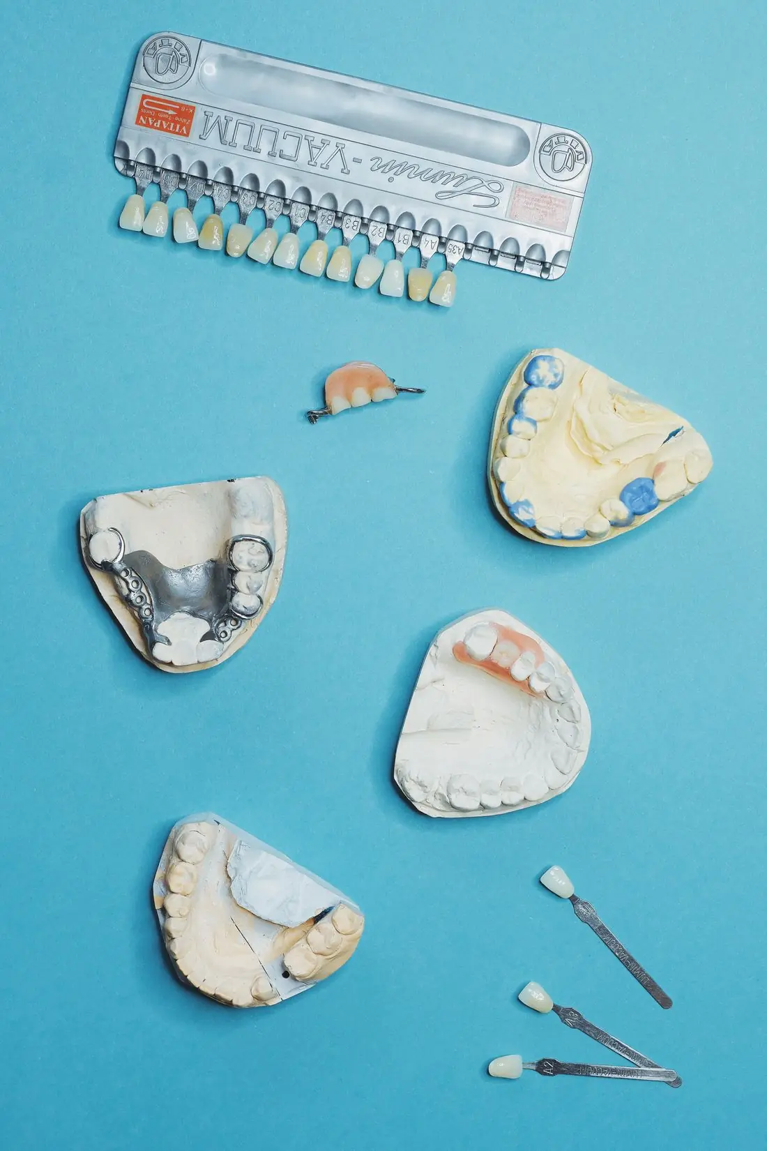 Modelos de gesso, estrutura metálica de prótese parcial e escala de cor de dentes sobre fundo azul